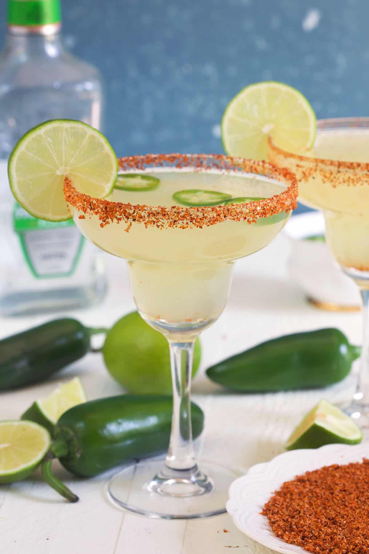 A glass of jalapeno margarita is placed next to several jalapenos. 