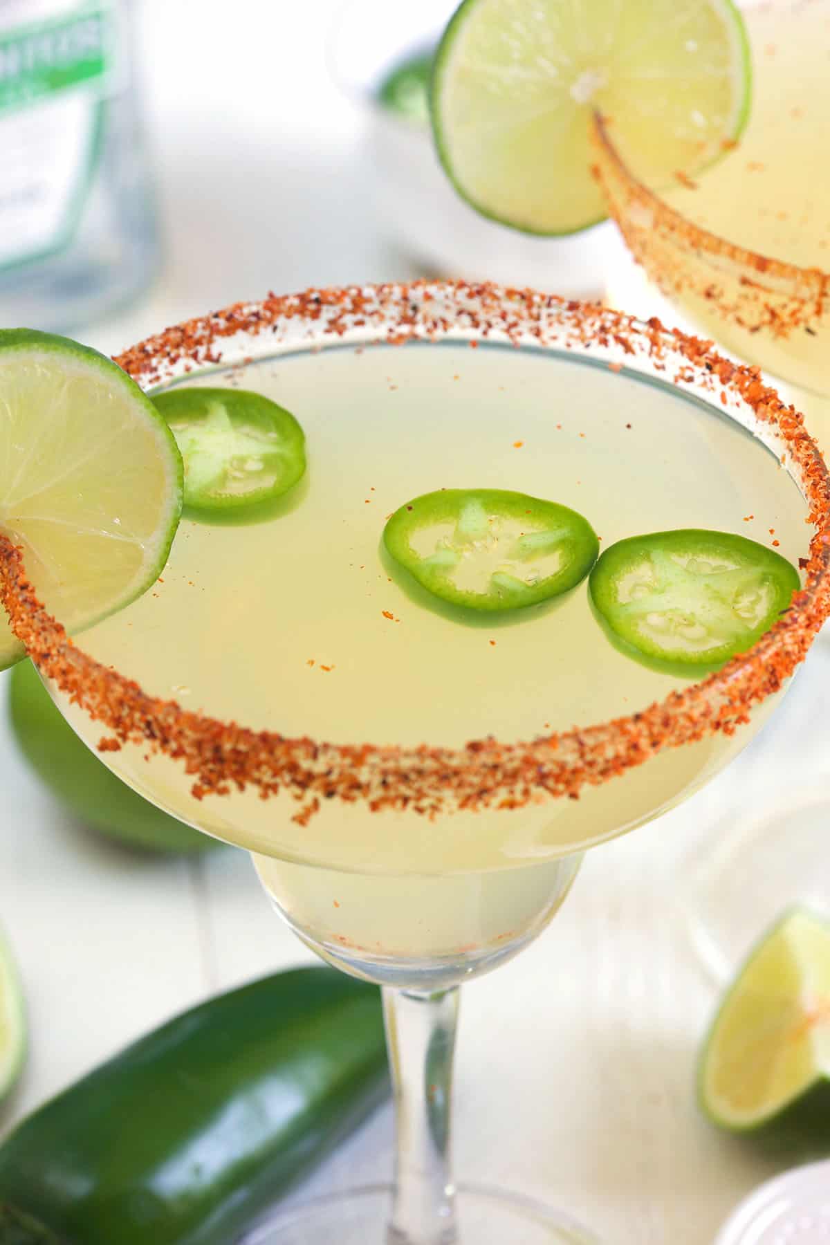 Three jalapeno slices are floating at the top of a margarita glass.