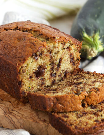 Chocolate Chip Zucchini Banana Bread loaf on an olive wood board with two slices in front of it.