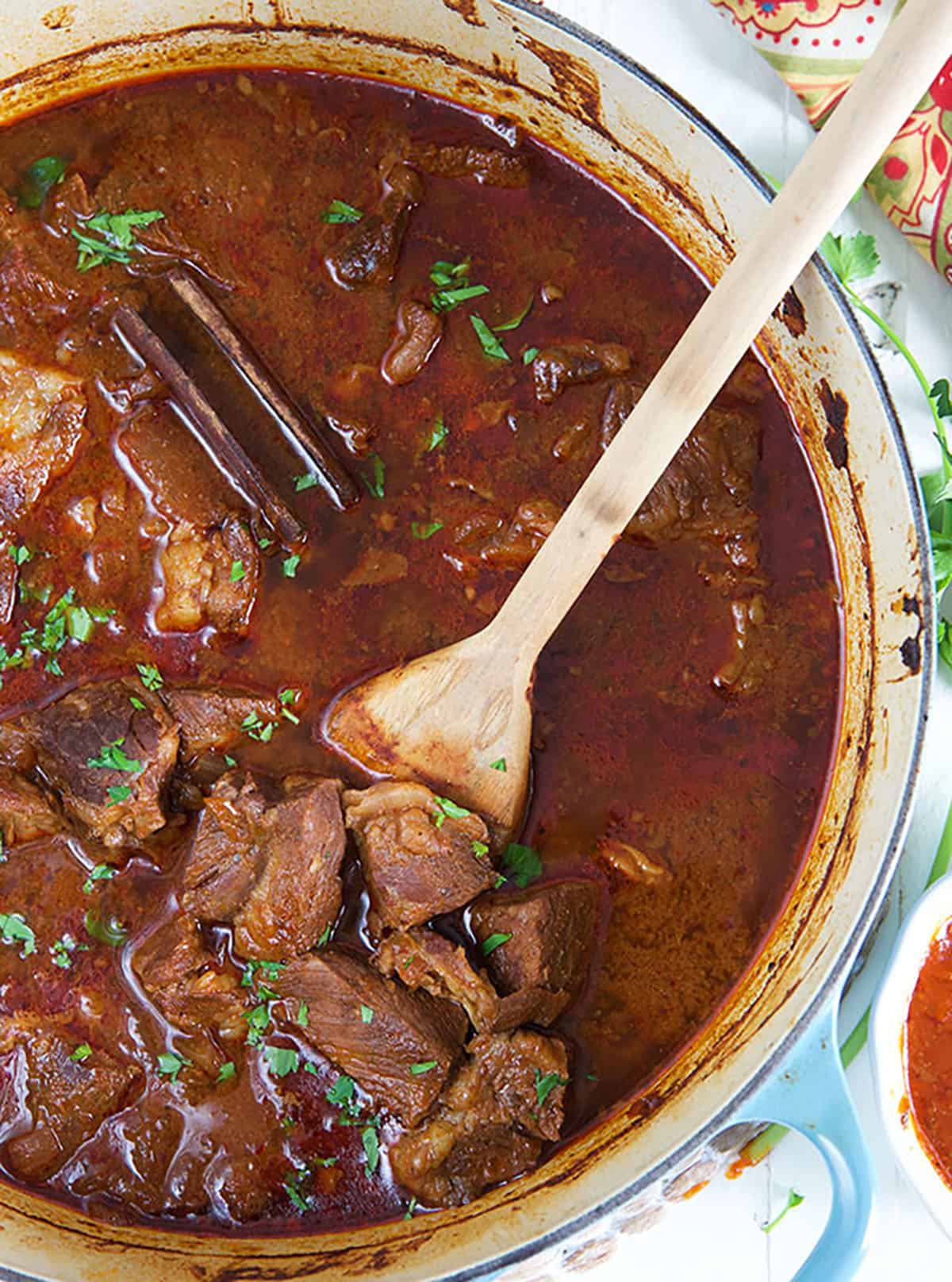 Birria Stew in a large blue pot with a wooden spoon.
