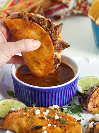 Birria Taco being dipped in a blue bowl of Birria stew.