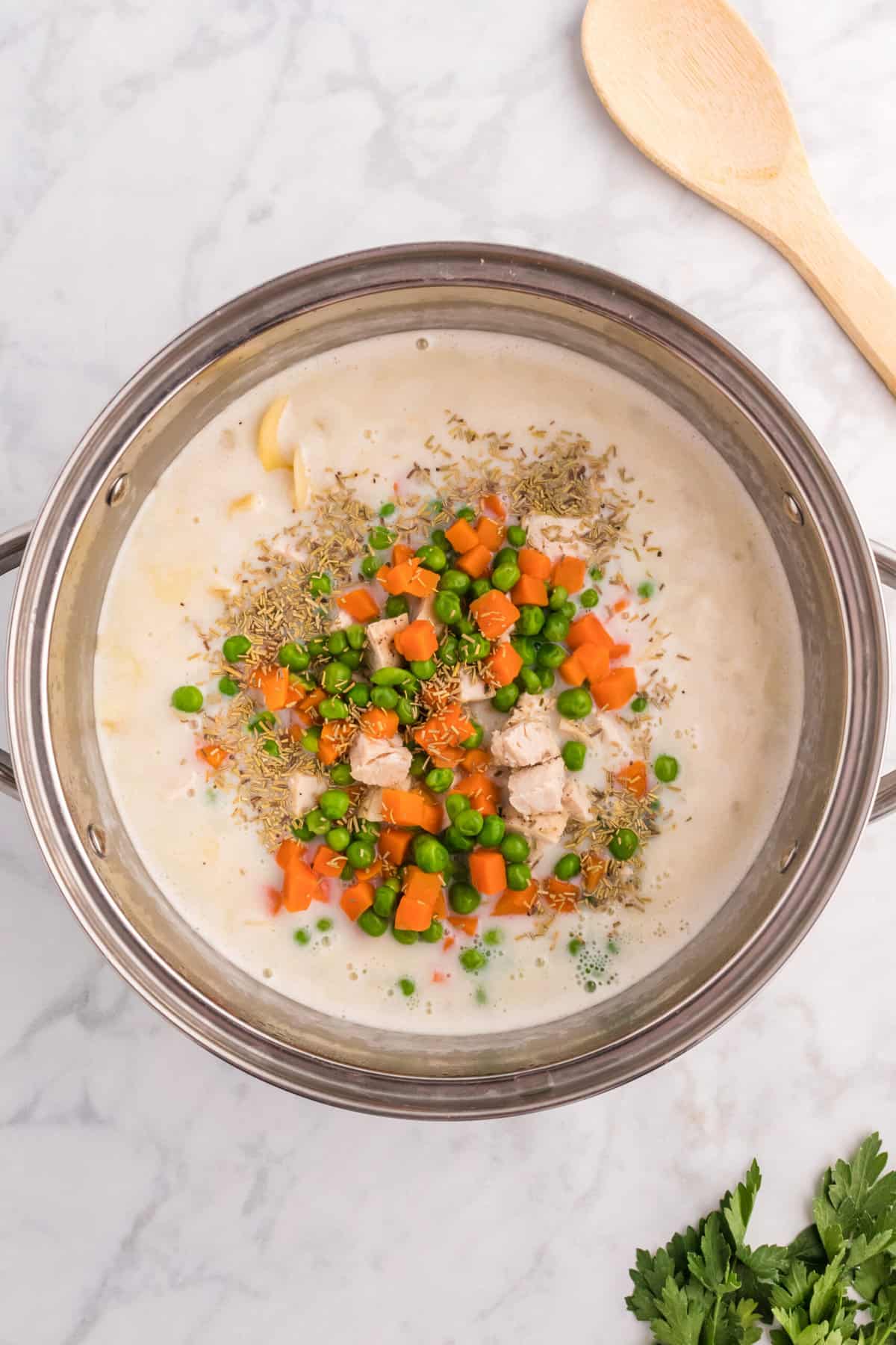 A pot of soup is topped with all of the ingredients like chicken and veggies that have yet to be stirred into the broth.