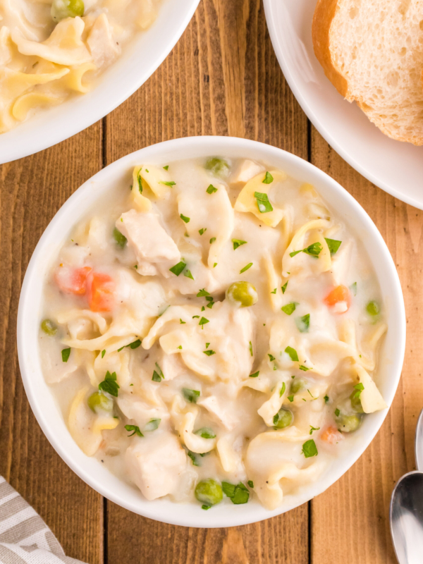 Bowls of creamy chicken noodle soup are placed on a wooden surface.