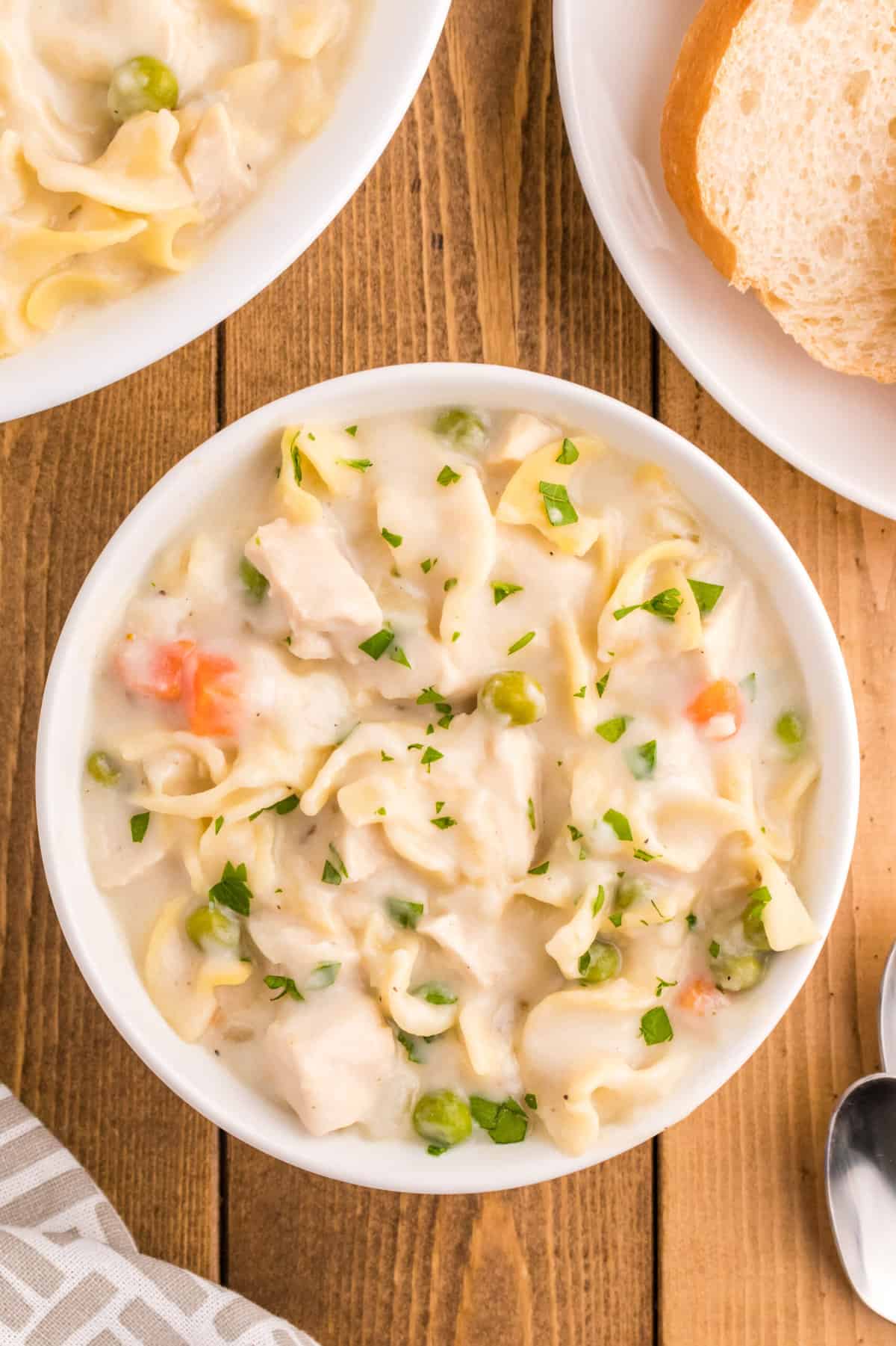 Bowls of creamy chicken noodle soup are placed on a wooden surface.