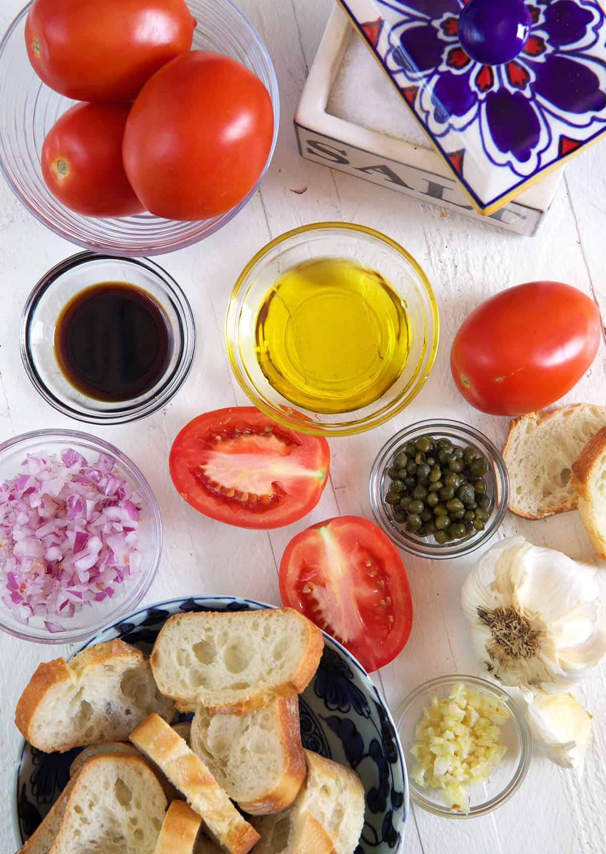 The ingredients for homemade bruschetta are placed on a white surface.