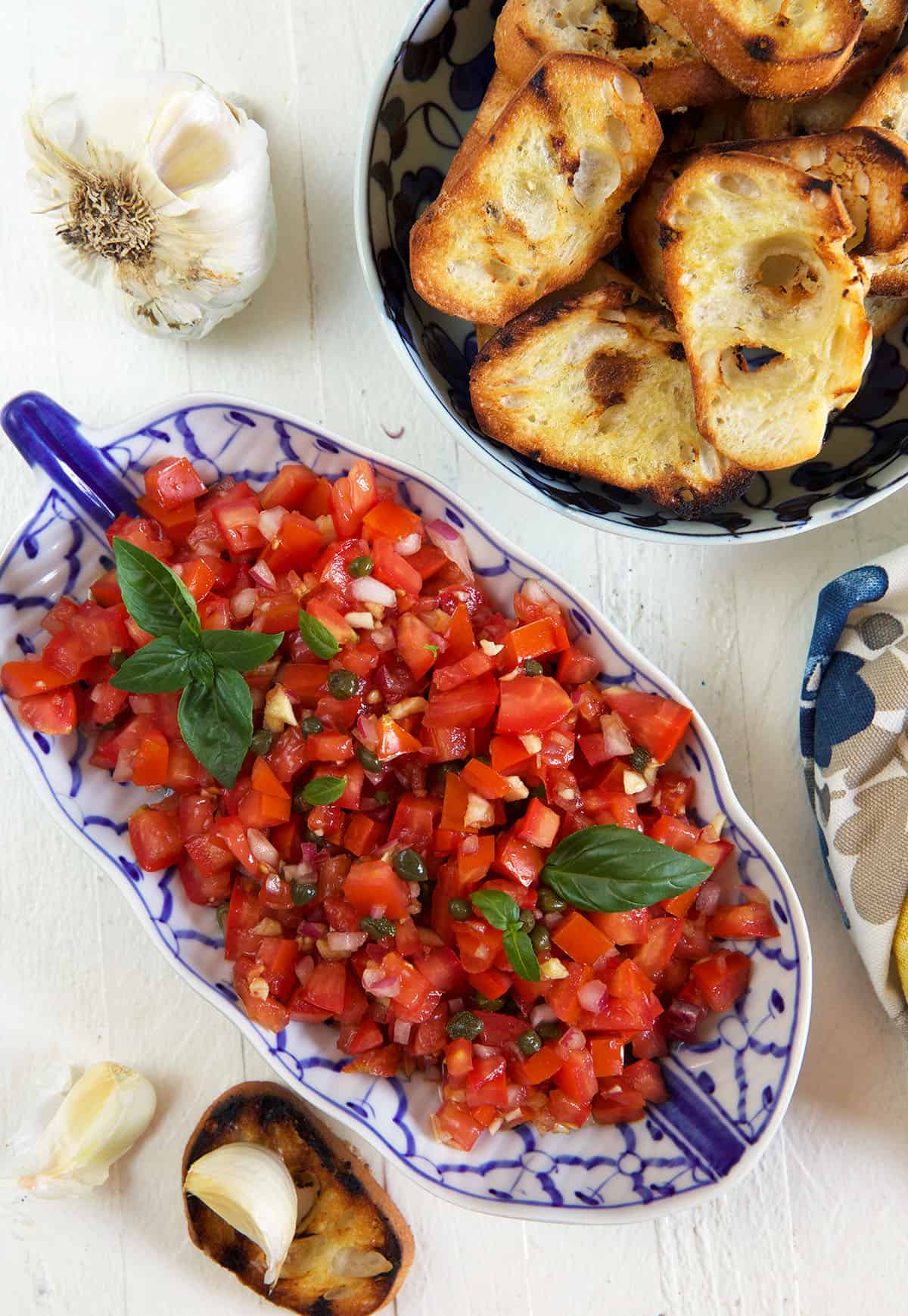 A large serving bowl of bruschetta is placed next to a bowl of toasted crostini.
