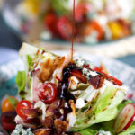 Loaded iceberg wedge salad with a balsamic glaze being drizzled on top