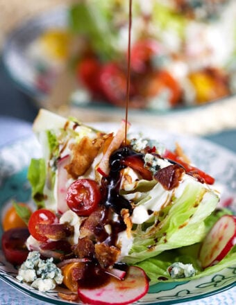 Loaded iceberg wedge salad with a balsamic glaze being drizzled on top