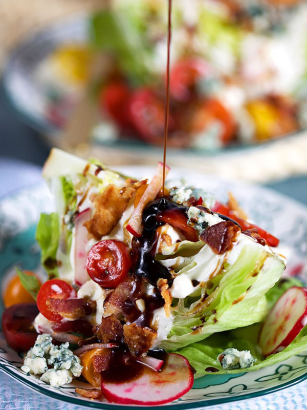 Loaded iceberg wedge salad with a balsamic glaze being drizzled on top