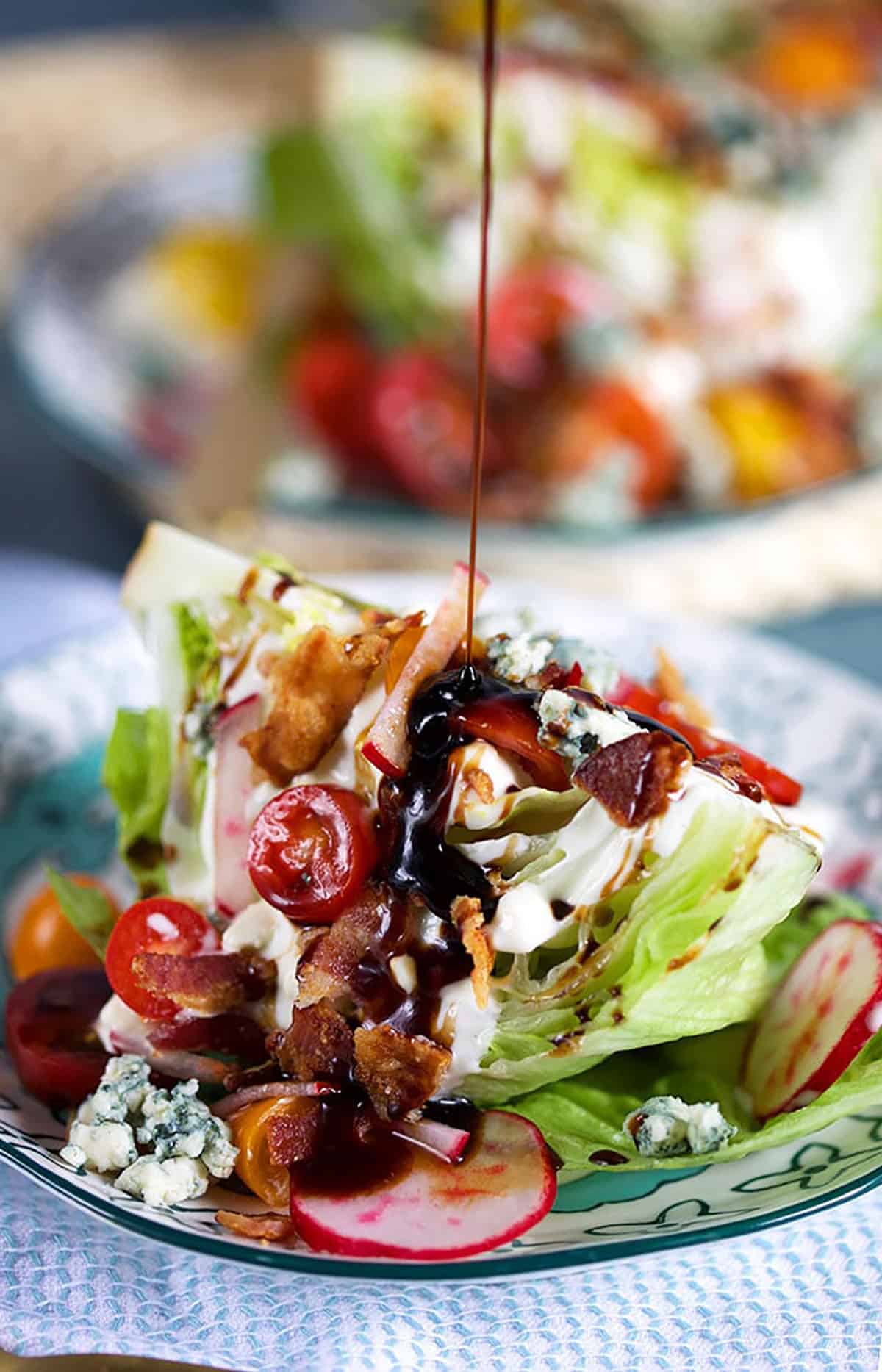 Loaded iceberg wedge salad with a balsamic glaze being drizzled on top 