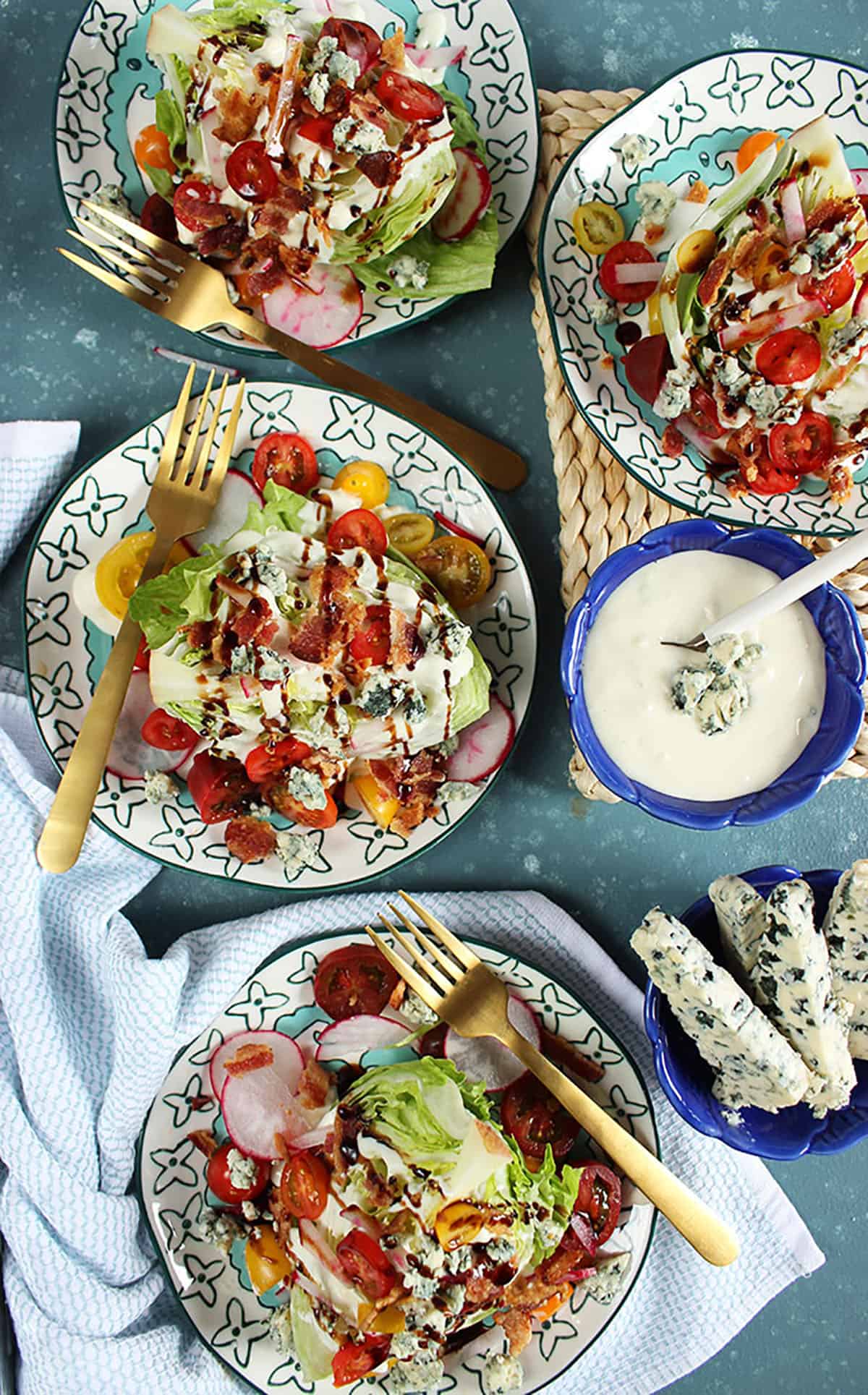Overhead shot of three iceberg wedge salads with a bowl of blue cheese dressing on the side. 