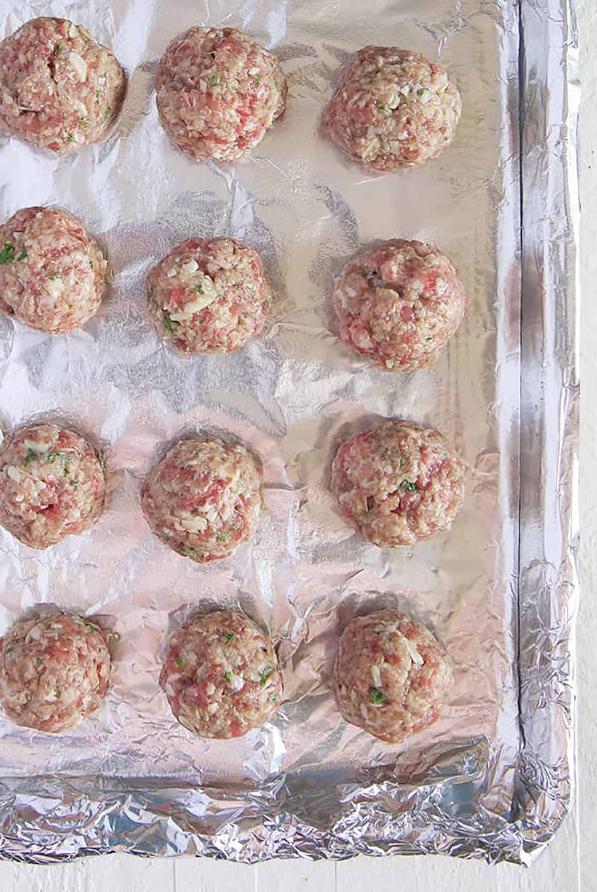 Raw meatballs ready for the oven on a baking sheet with foil.