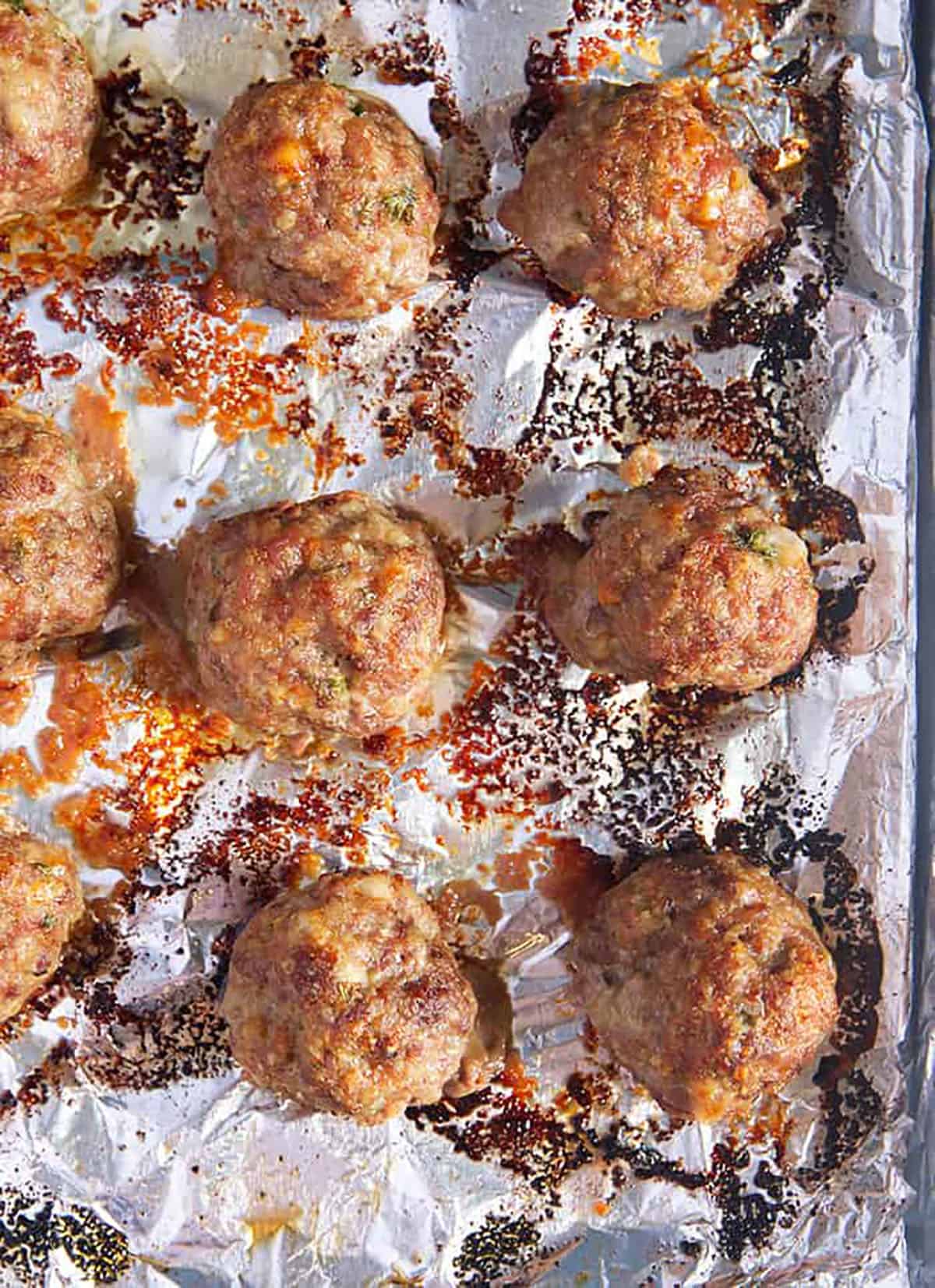 Baked meatballs on a baking sheet with foil.