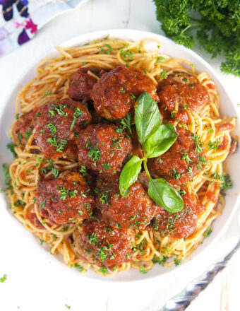 spaghetti and baked meatballs in a white bowl on a white background.
