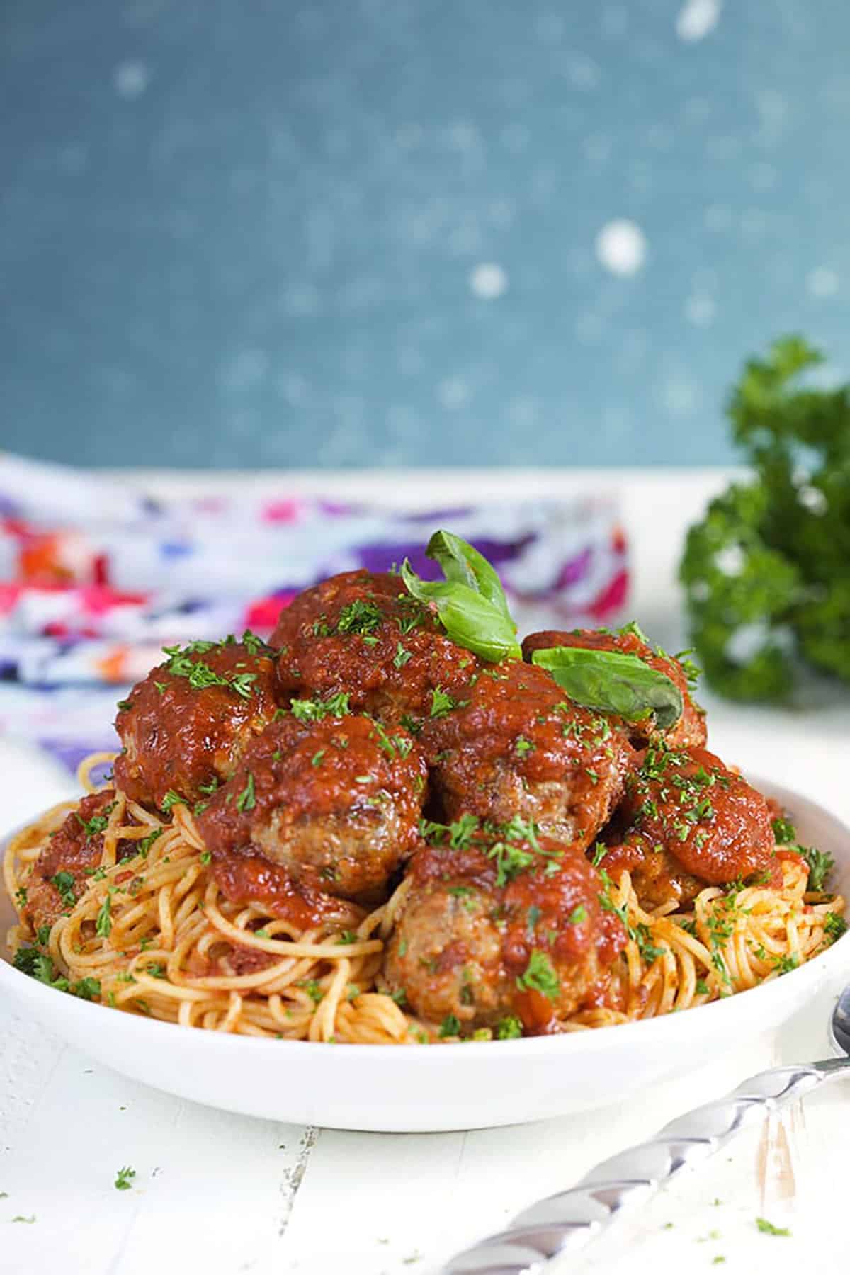 Baked meatballs on top of spaghetti in a white bowl with a blue and white background.
