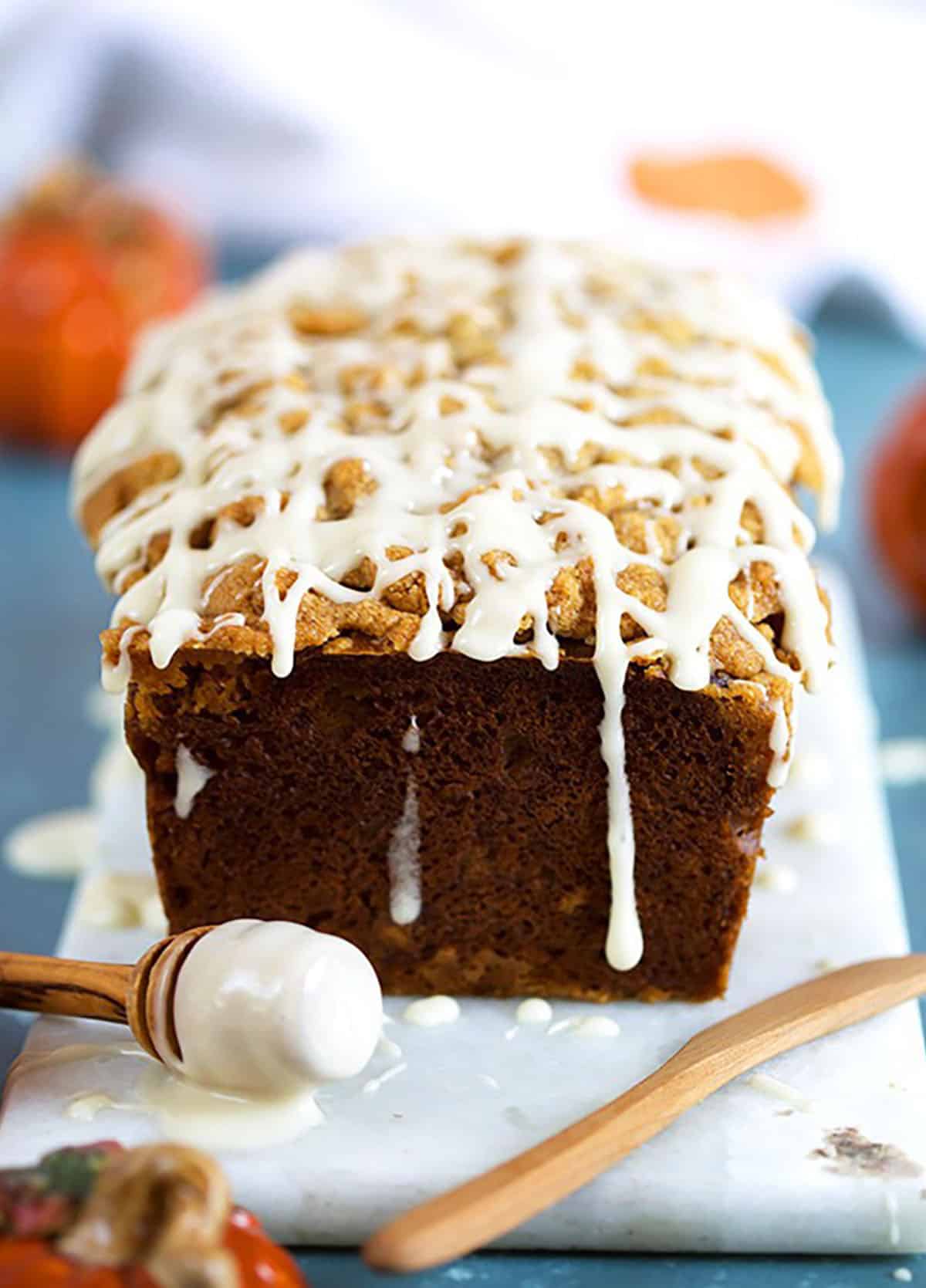 Maple Glazed Pumpkin Banana Bread with drizzle on a white board on a blue background