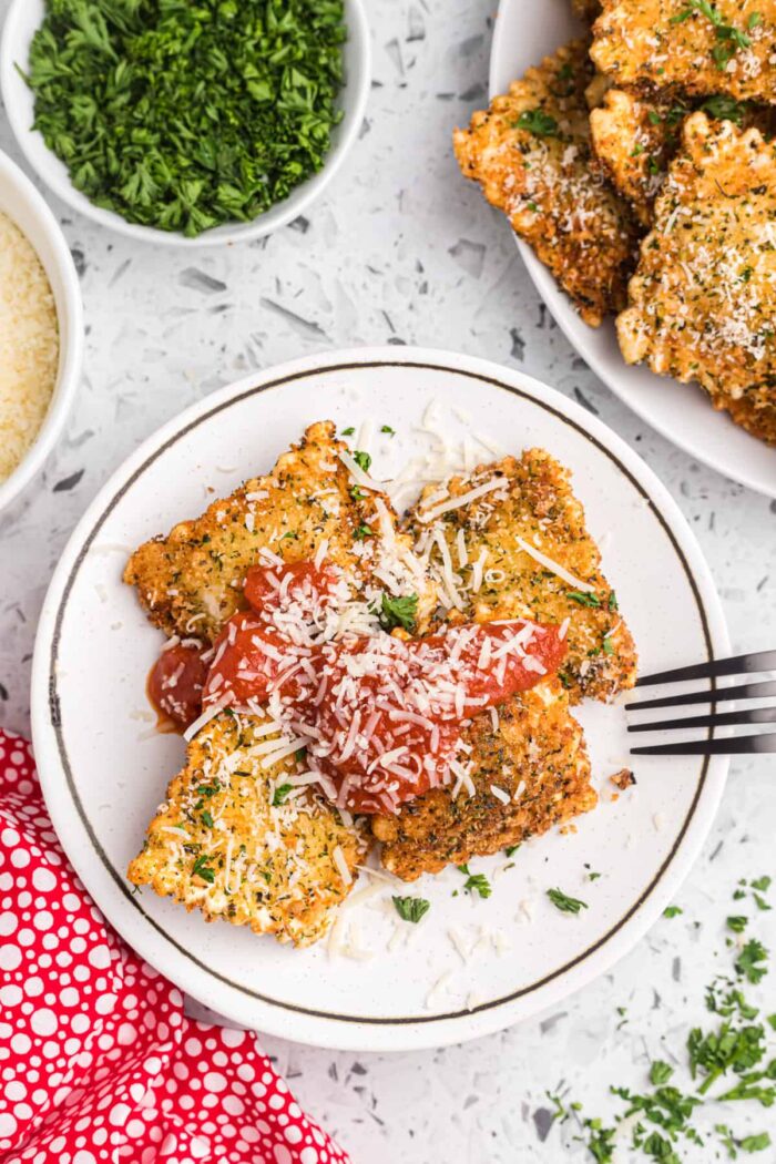 Fried ravioli on a plate is topped with red sauce and parmesan.