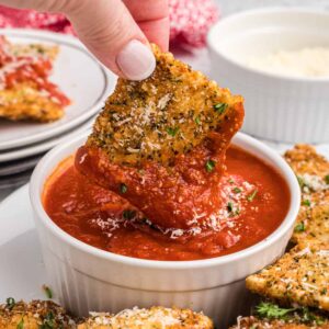 A fried ravioli is being dunked into marinara sauce.