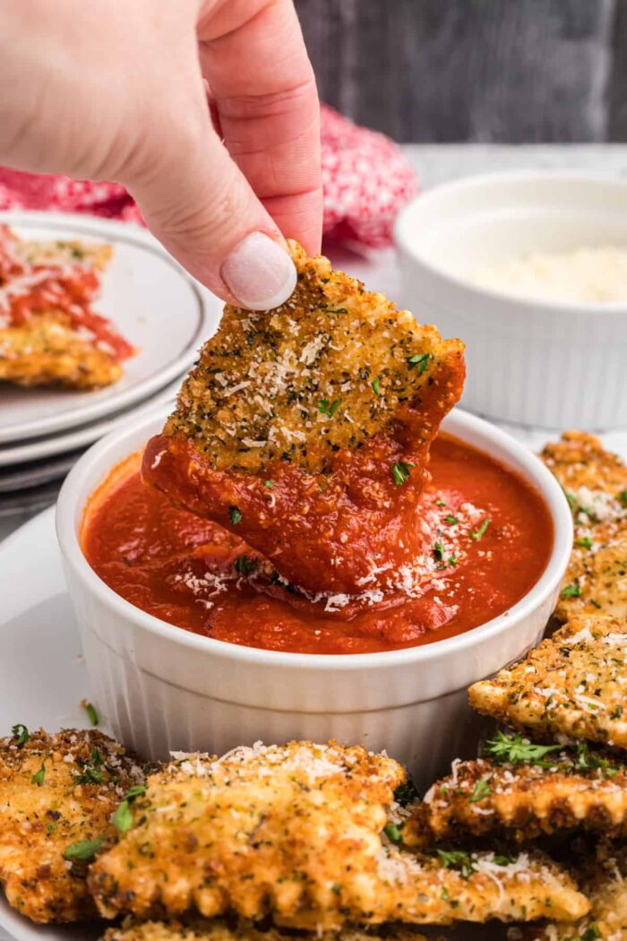 A fried ravioli is being dunked into marinara sauce.