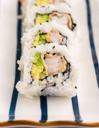 A sliced shrimp tempura roll is placed on a striped white and blue plate.