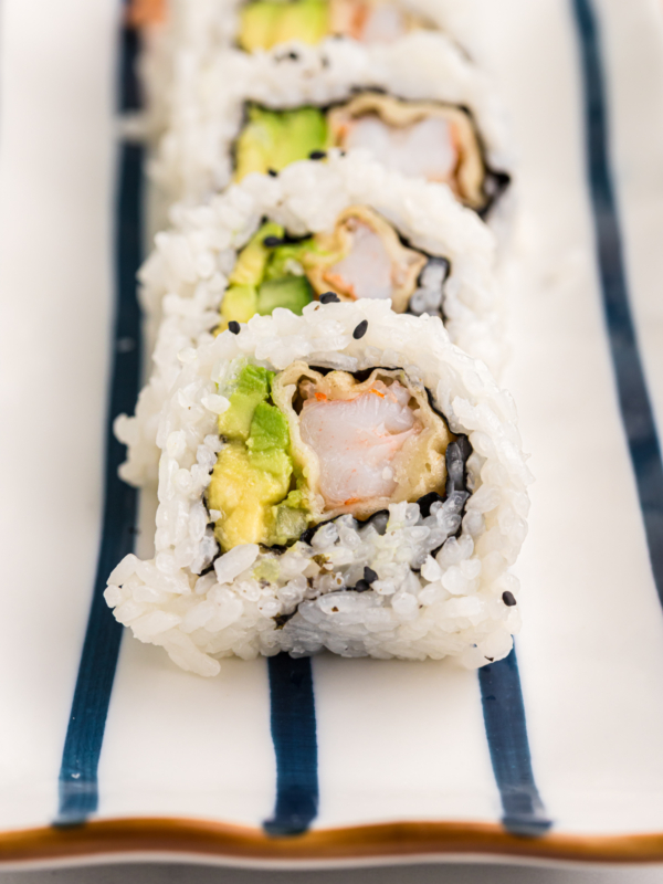 A sliced shrimp tempura roll is placed on a striped white and blue plate.