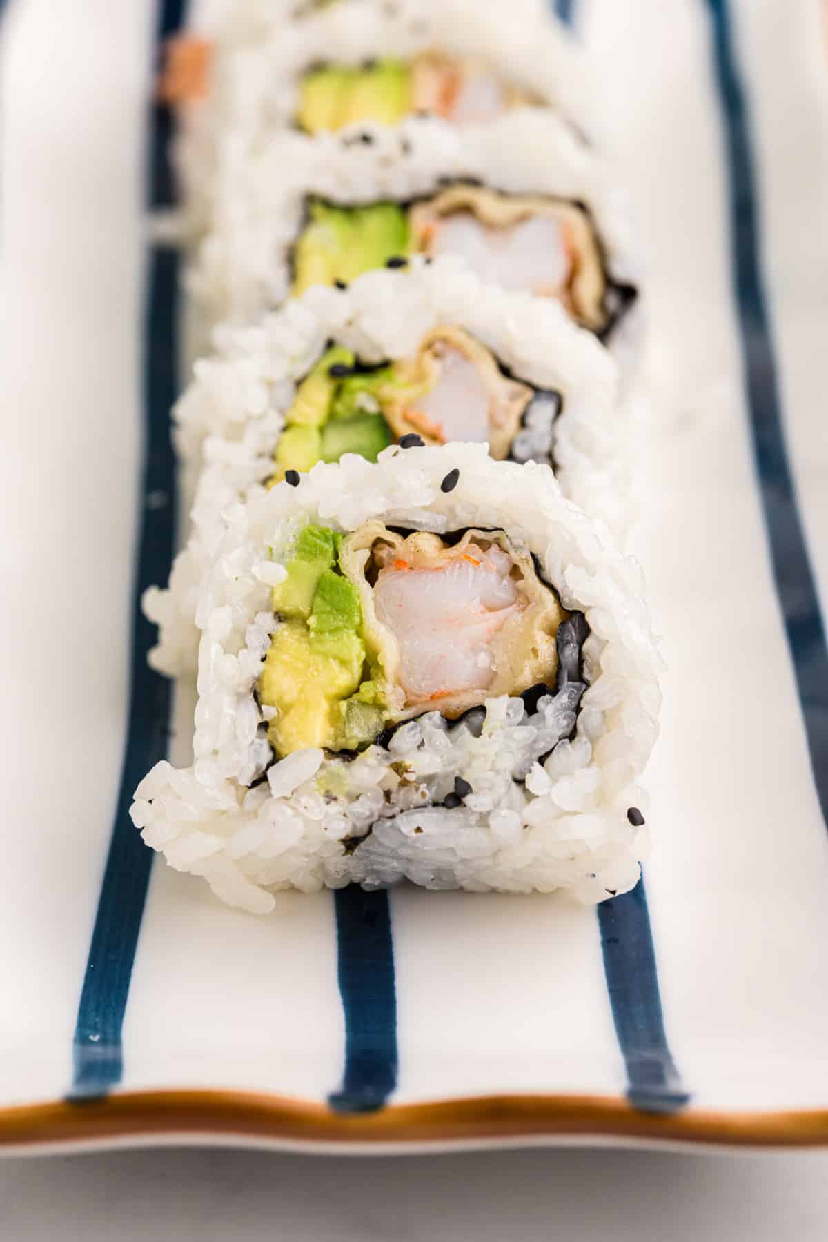 A sliced shrimp tempura roll is placed on a striped white and blue plate.