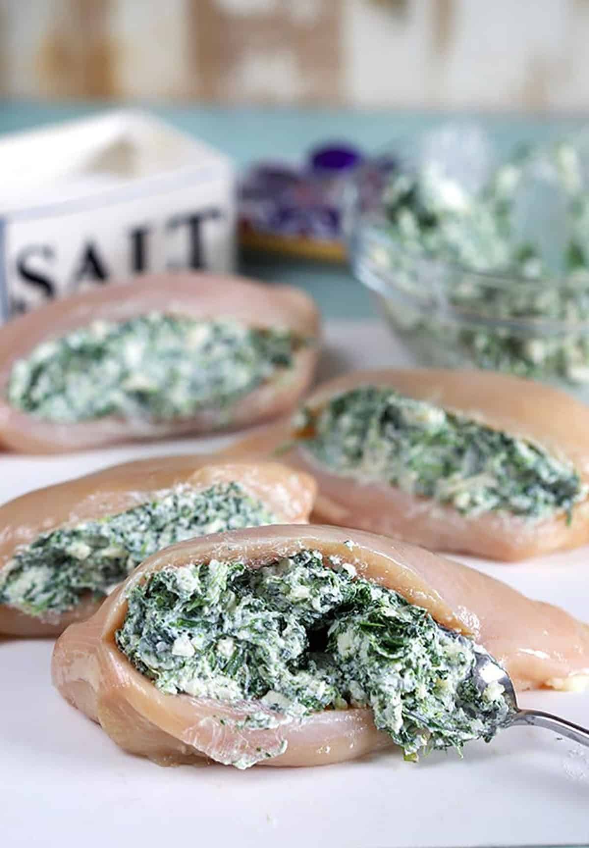Process shot of spinach dip being stuffed into a chicken breast.