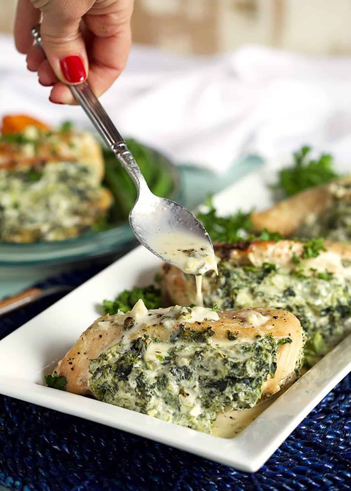Spinach and cheese stuffed chicken breasts with a spoonful of garlic parmesan sauce drizzled overtop.