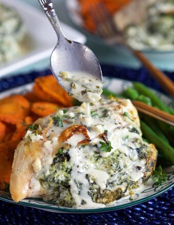 Close up of Spinach Stuffed Chicken being drizzled with parmesan garlic sauce with a silver spoon.