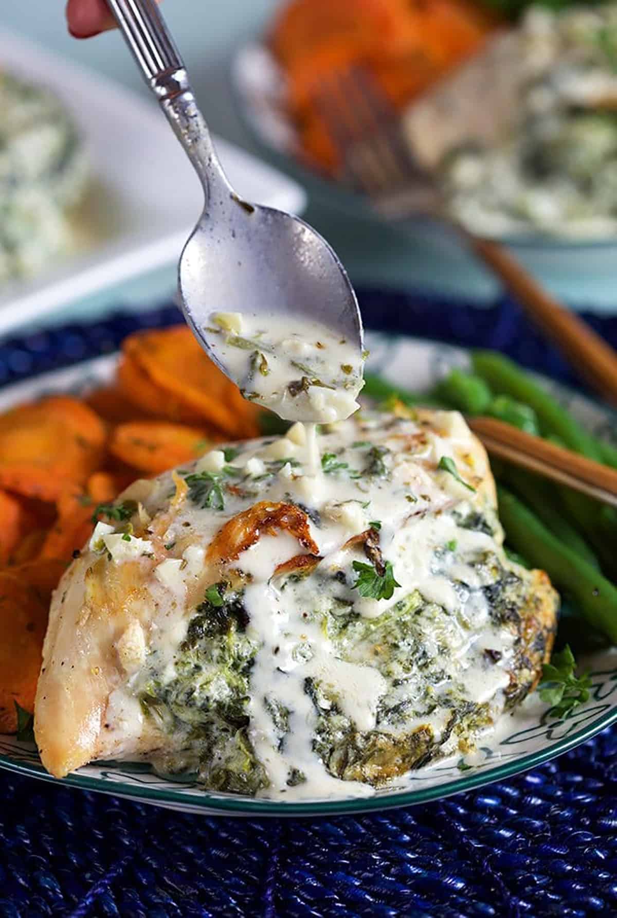Close up of Spinach Stuffed Chicken being drizzled with parmesan garlic sauce with a silver spoon.
