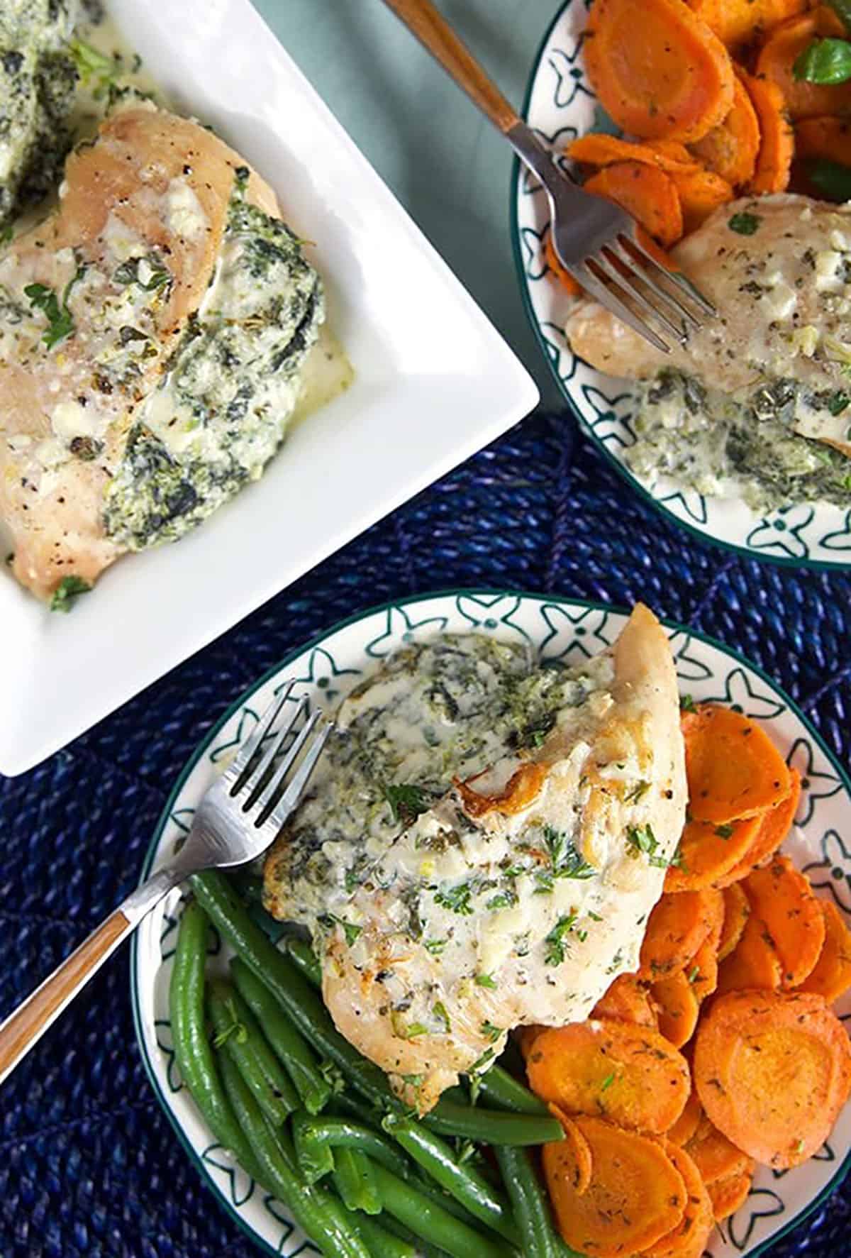 Overhead shot of spinach stuffed chicken breasts on plates with carrots and green beans.