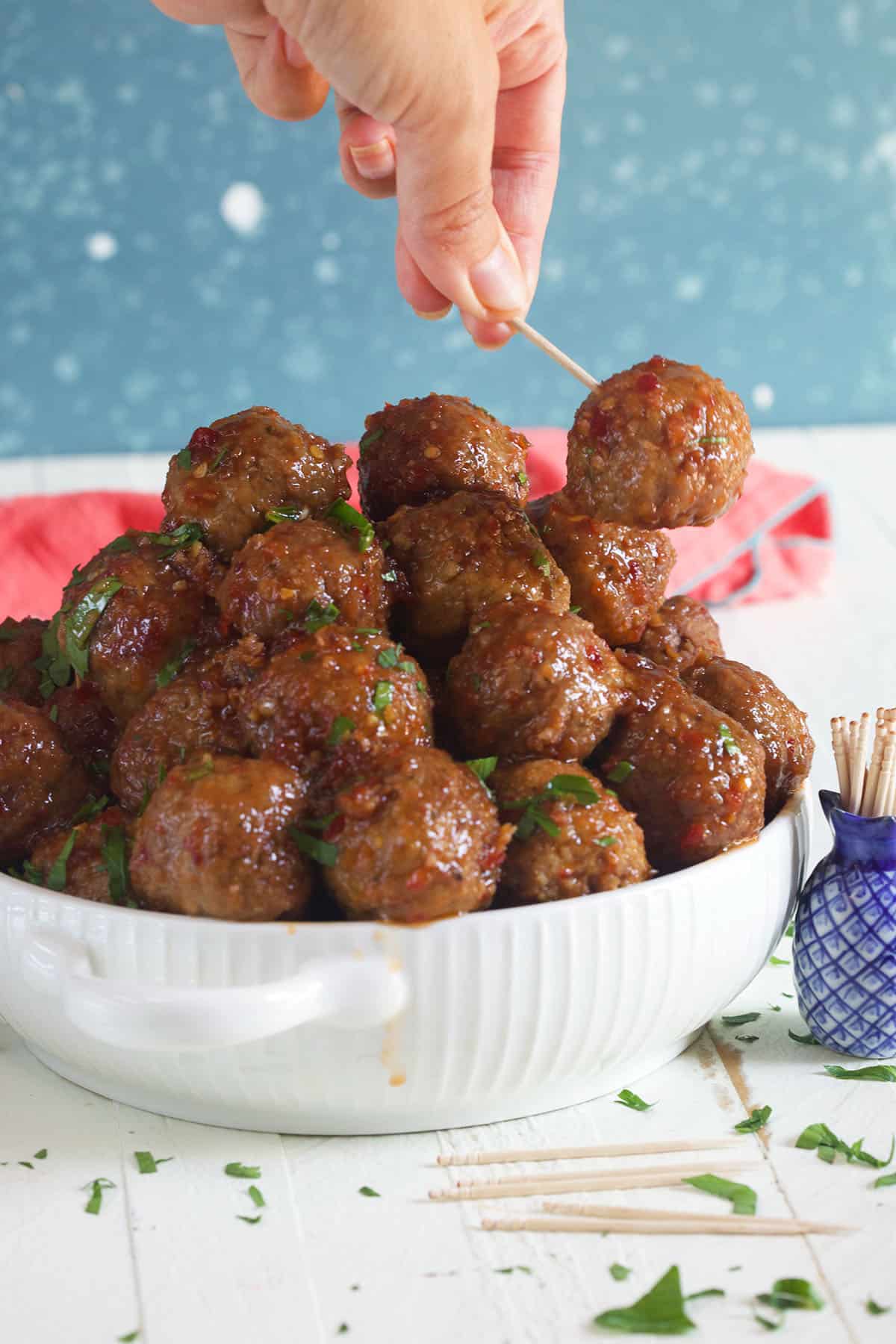 A hand is lifting a meatball from a full bowl using a toothpick. 