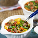 Vegetable Beef Soup in a white bowl with a blue handled spoon.