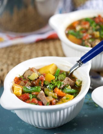 Vegetable Beef Soup in a white bowl with a blue handled spoon.