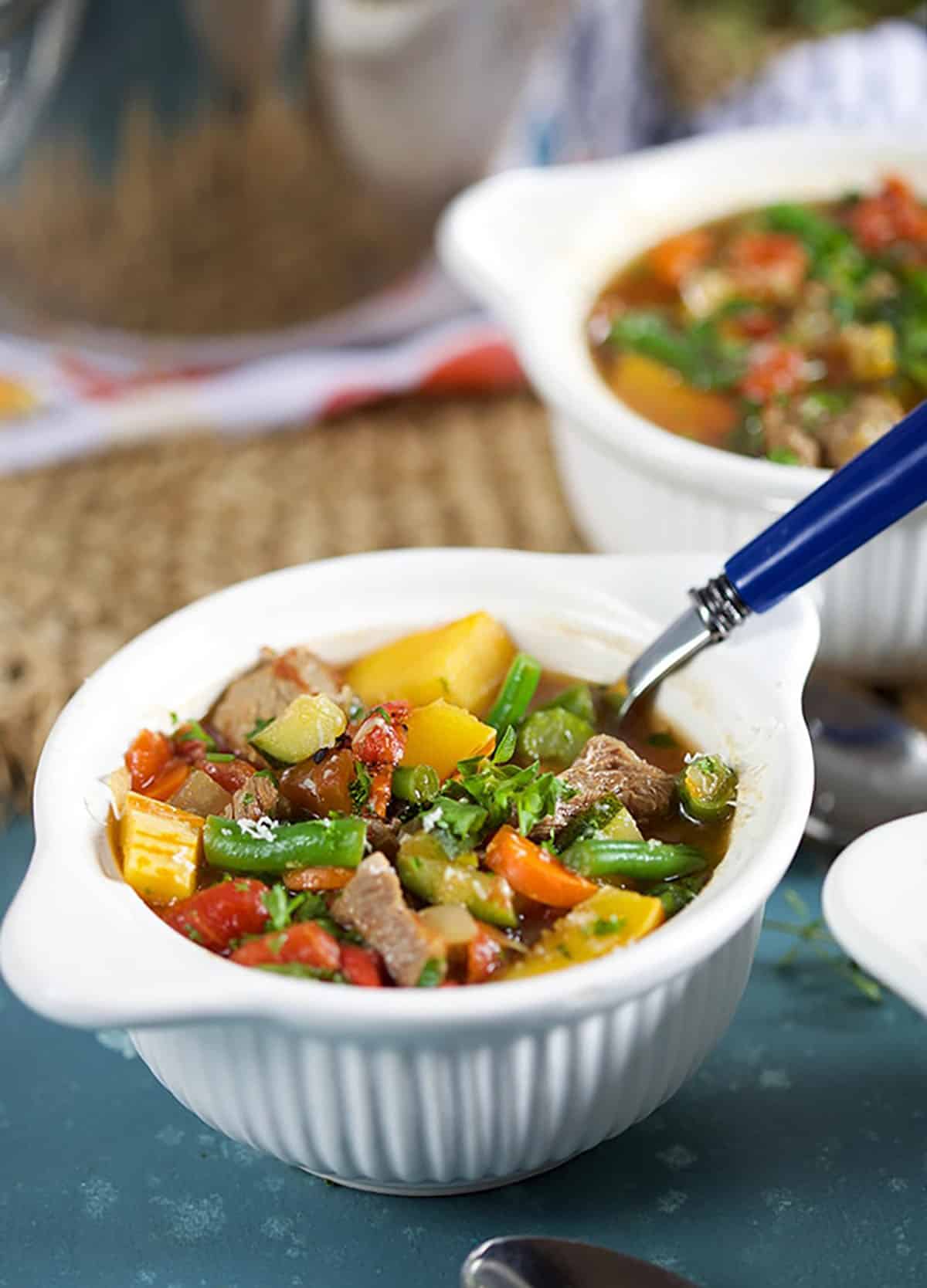 Vegetable Beef Soup in a white bowl with a blue handled spoon.