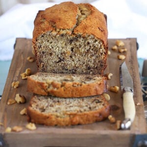 Banana Nut Bread on a wood tray with two slices and a knife.