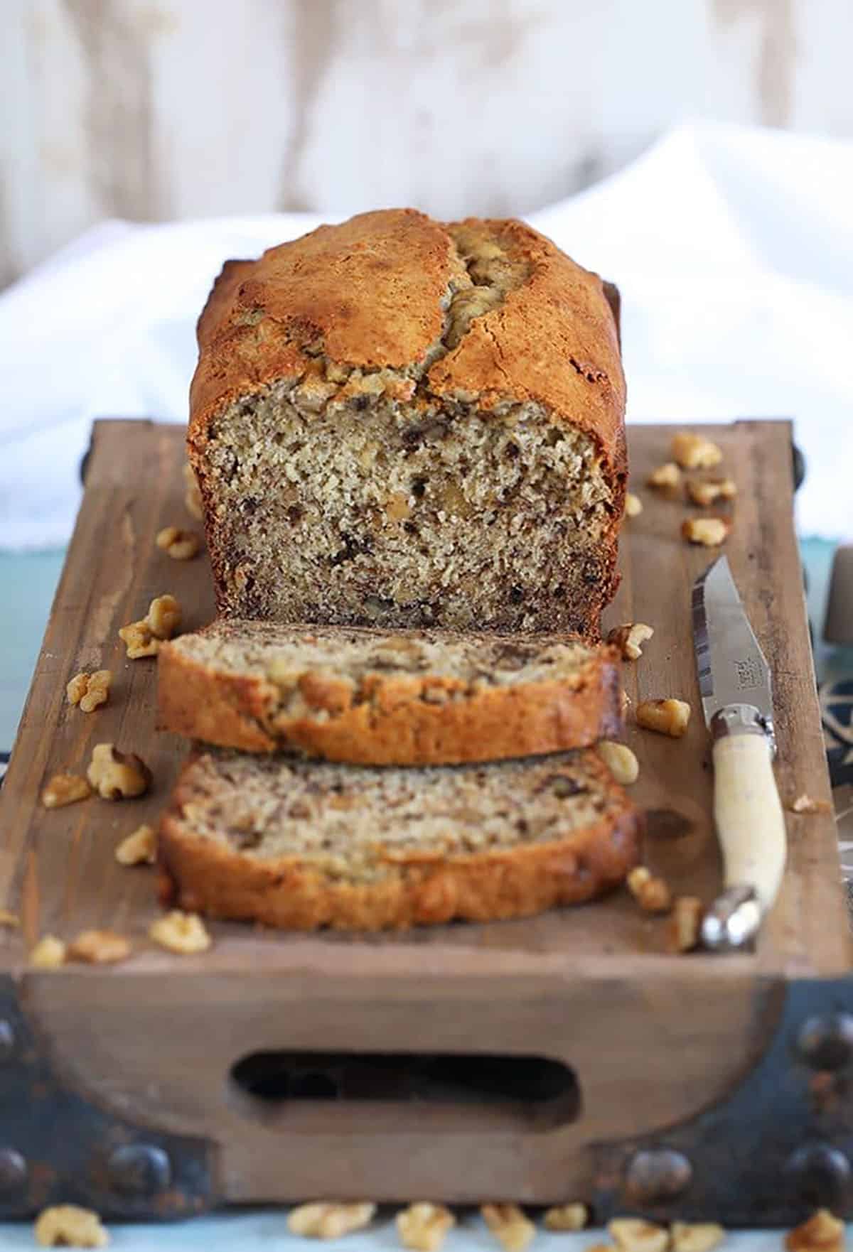 Banana Nut Bread on a wood tray with two slices and a knife.