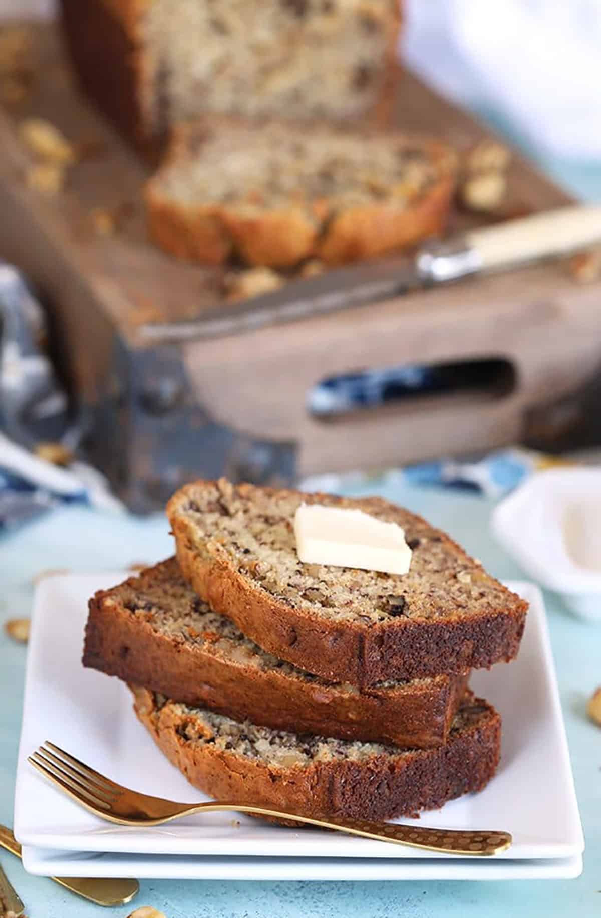 Banana Nut Bread sliced and stacked on a white plate with a pat of butter on top