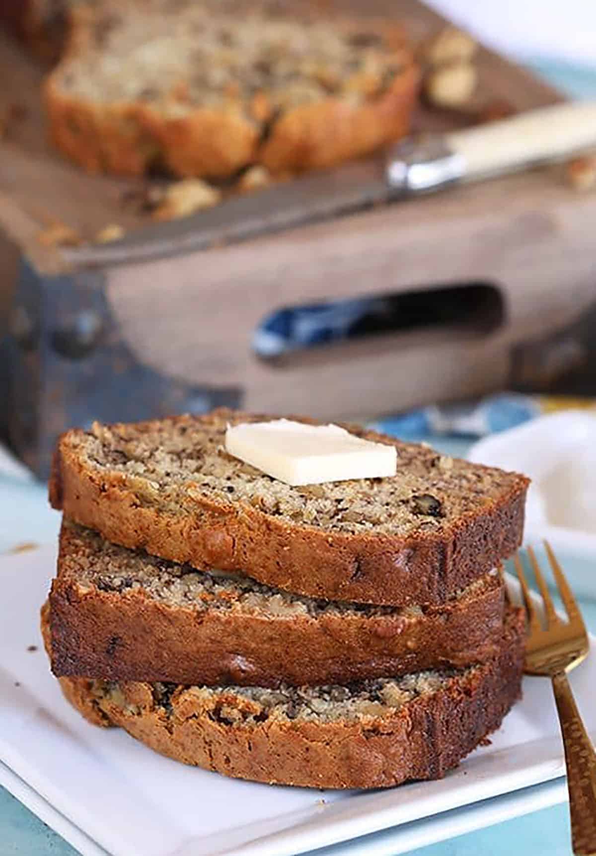 Three slices of banana nut bread stacked on a white plate