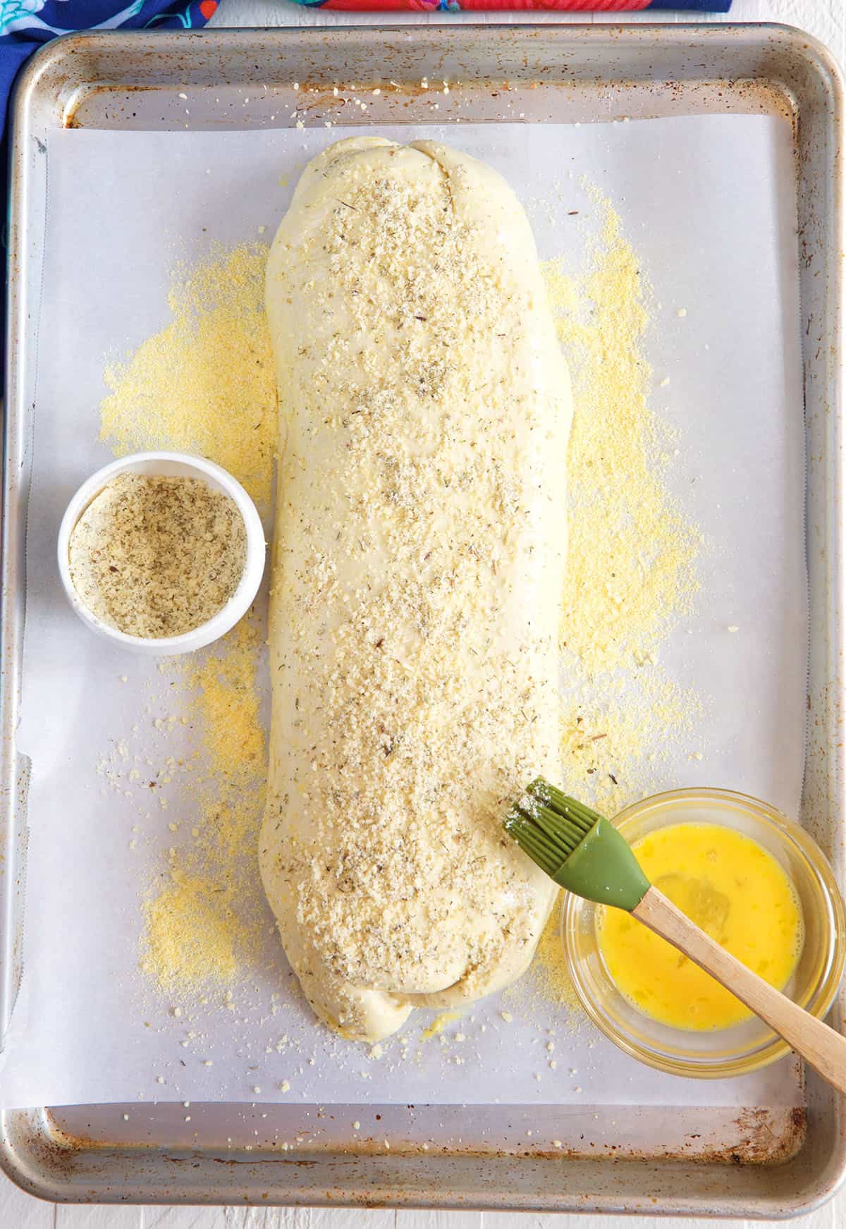 Butter and cheese are spread across the top of an uncooked stromboli.