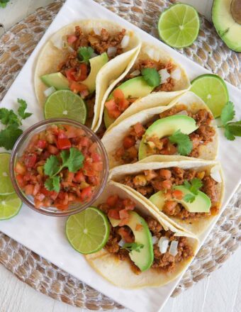 Salsa, tacos, and garnishes are all spread out across a white plate.