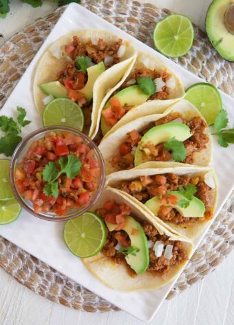 Salsa, tacos, and garnishes are all spread out across a white plate.