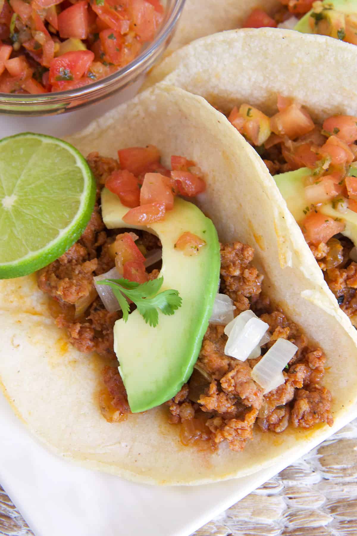 Avocado, tomatoes, and onions and limes are placed on top of a taco.
