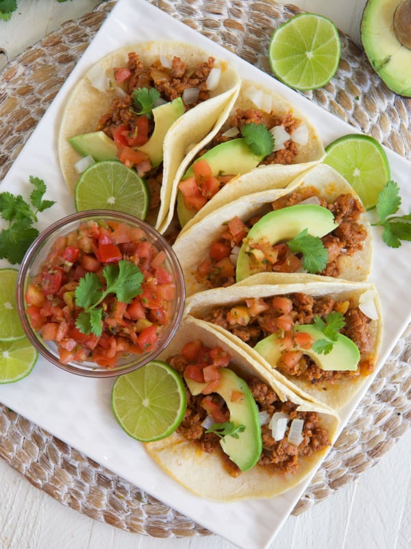 Salsa, tacos, and garnishes are all spread out across a white plate.