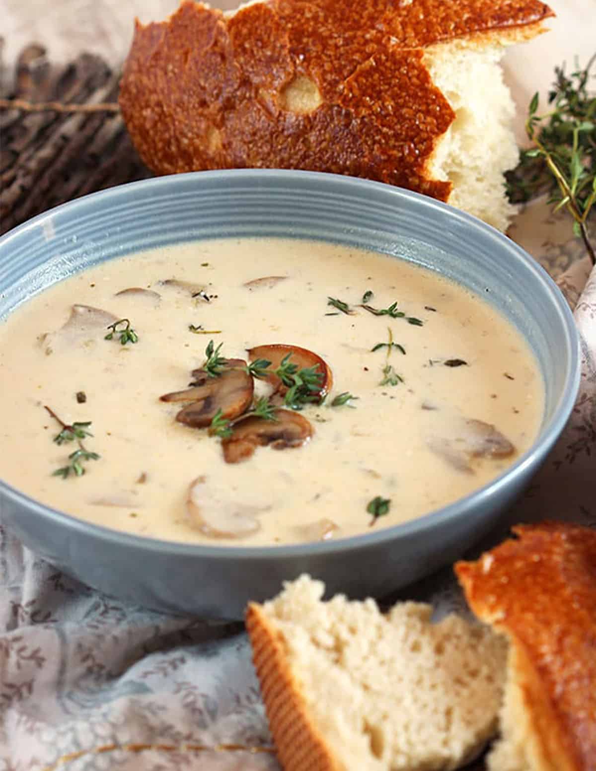 Cream of mushroom soup in a blue bowl with a loaf of sourdough bread