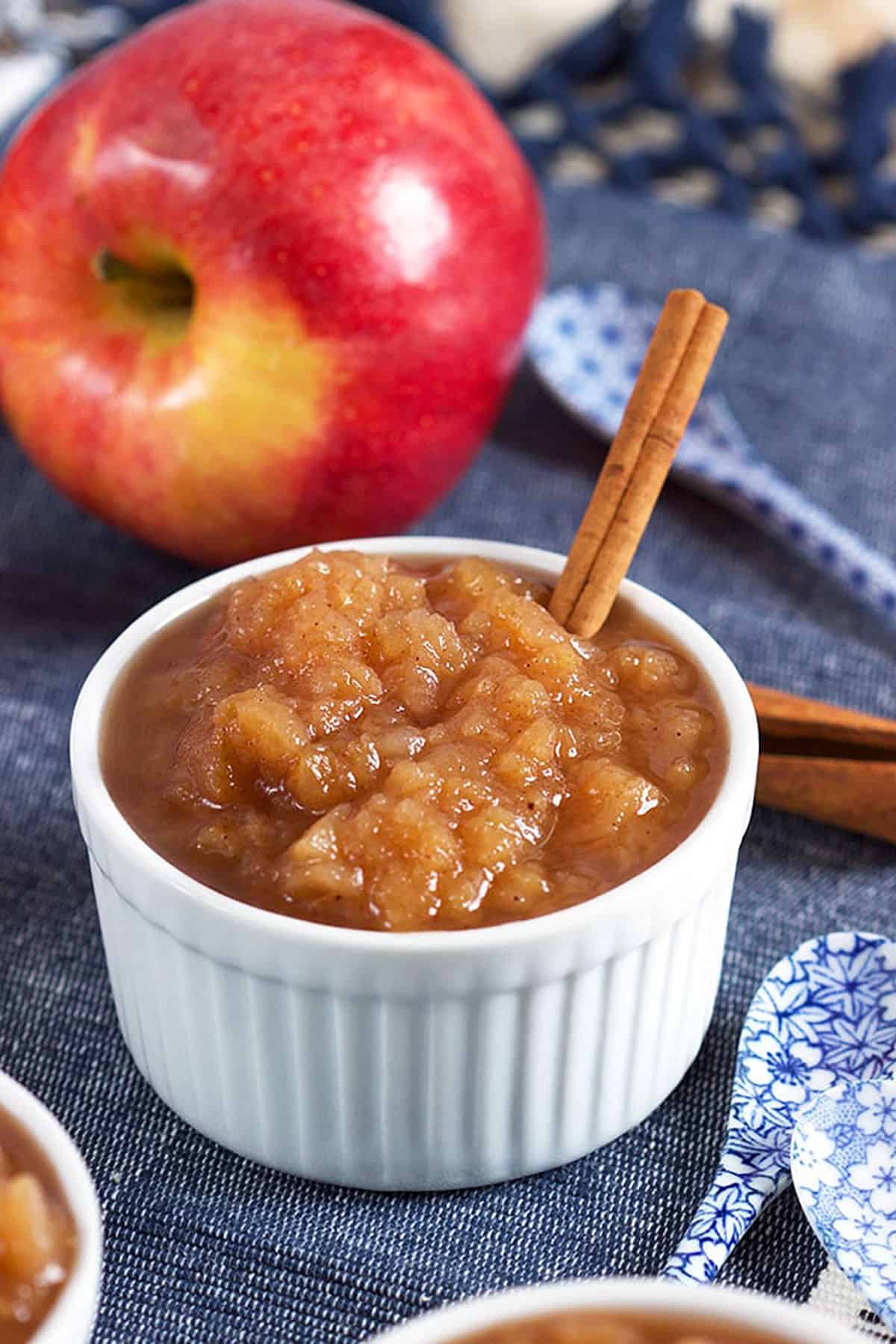 crock pot applesauce in a white bowl with a cinnamon stick and an apple in the background.