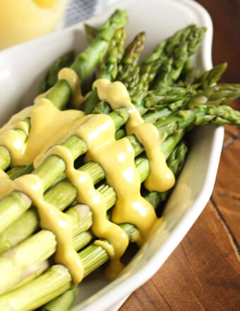 Hollandaise Sauce drizzled over asparagus in a white serving dish.