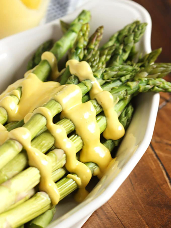 Hollandaise Sauce drizzled over asparagus in a white serving dish.