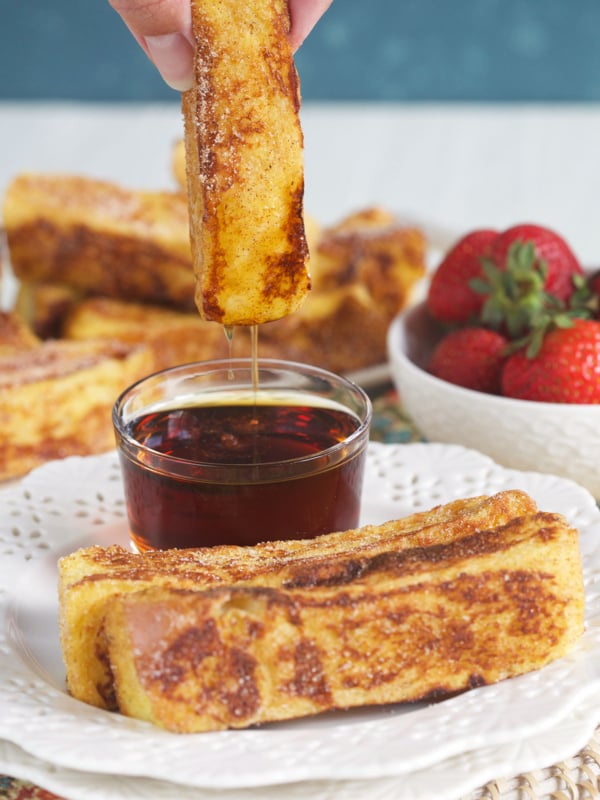A french toast stick is being dipped in maple syrup.