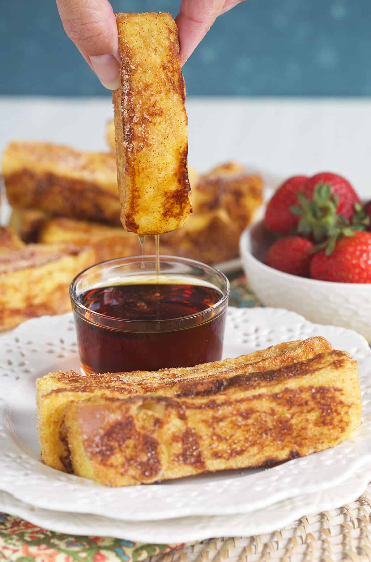 A french toast stick is being dipped in maple syrup.